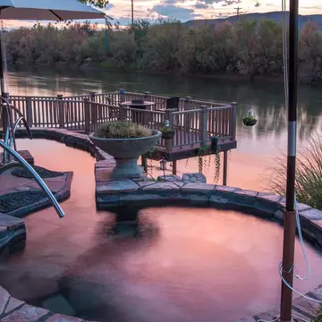 A small round pool right beside a river at sunset.