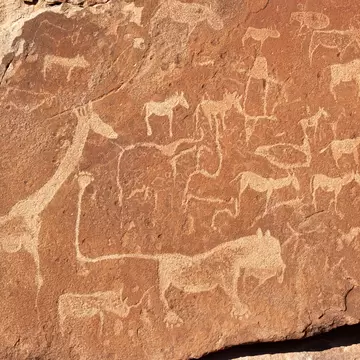 Pale outlines of animals, including a big cat with a long curled tail, pecked into red-brown rock