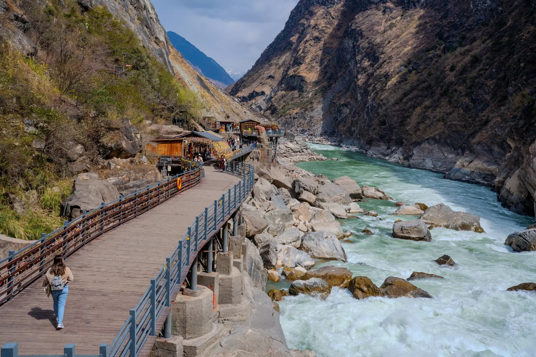 A woman walks along a riverside boardwalk through a gorge.