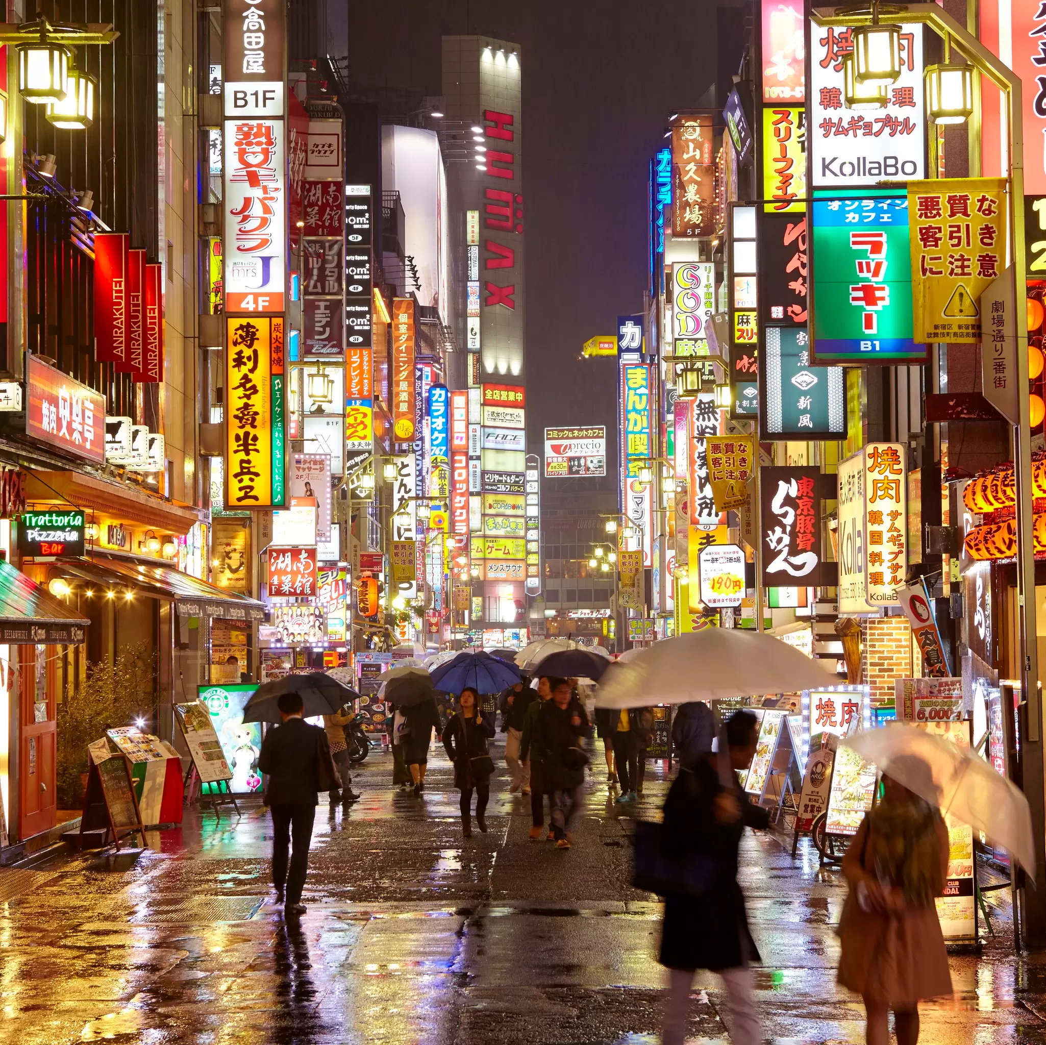 The neon-lit streets of Shinjuku in Tokyo, with shoppers in the rain beneath umbrellas.