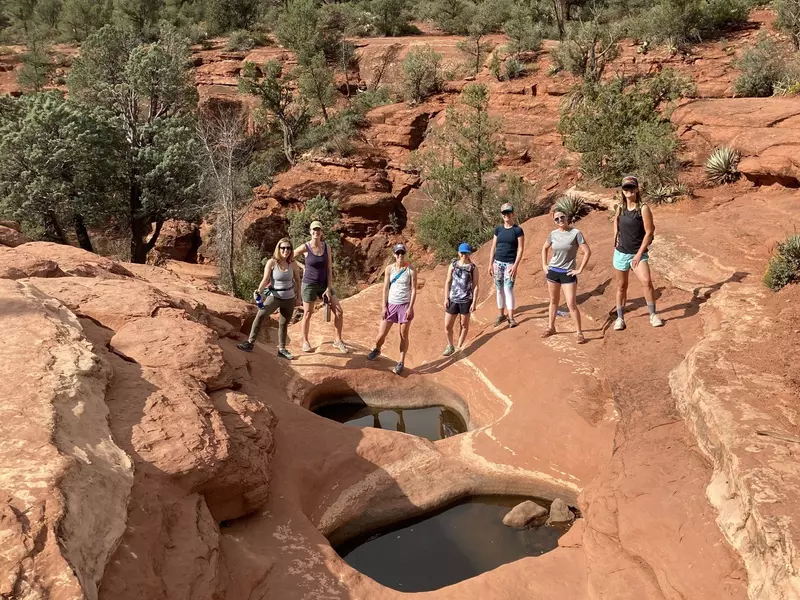 A group of seven women posing for a photo around a waterhole in a red, rocky landscape 