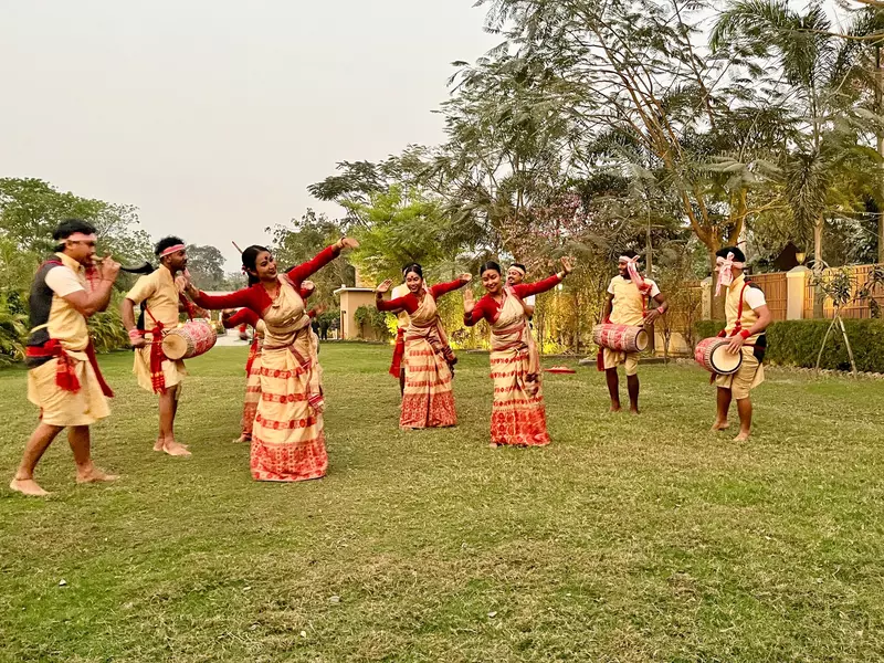 A group of dancers and drummers wearing red and gold perform in a garden.