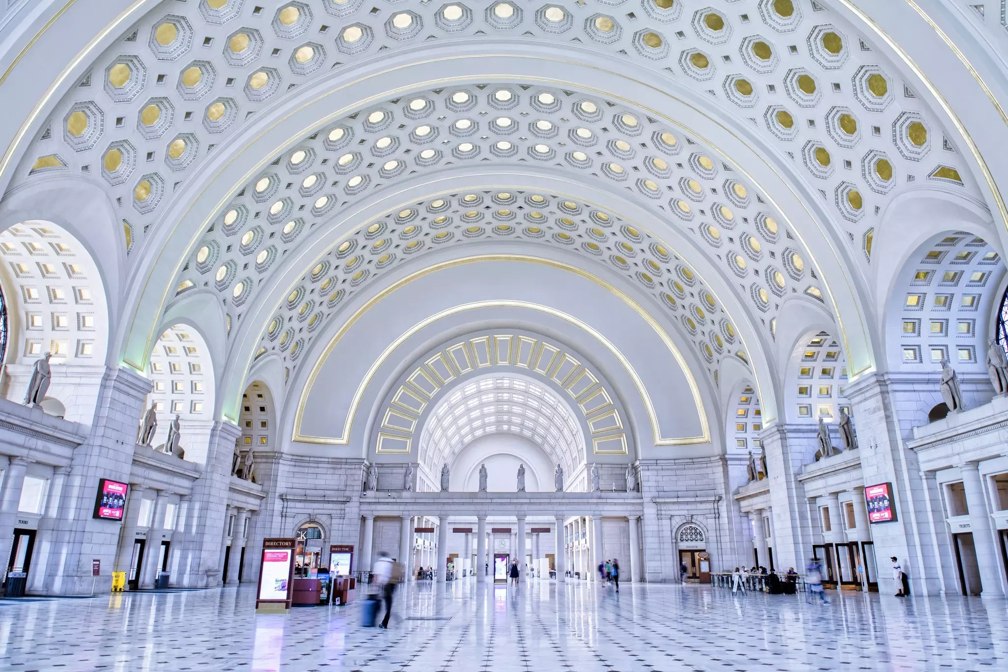 The stark white interior of a large train station with an arched ceiling.