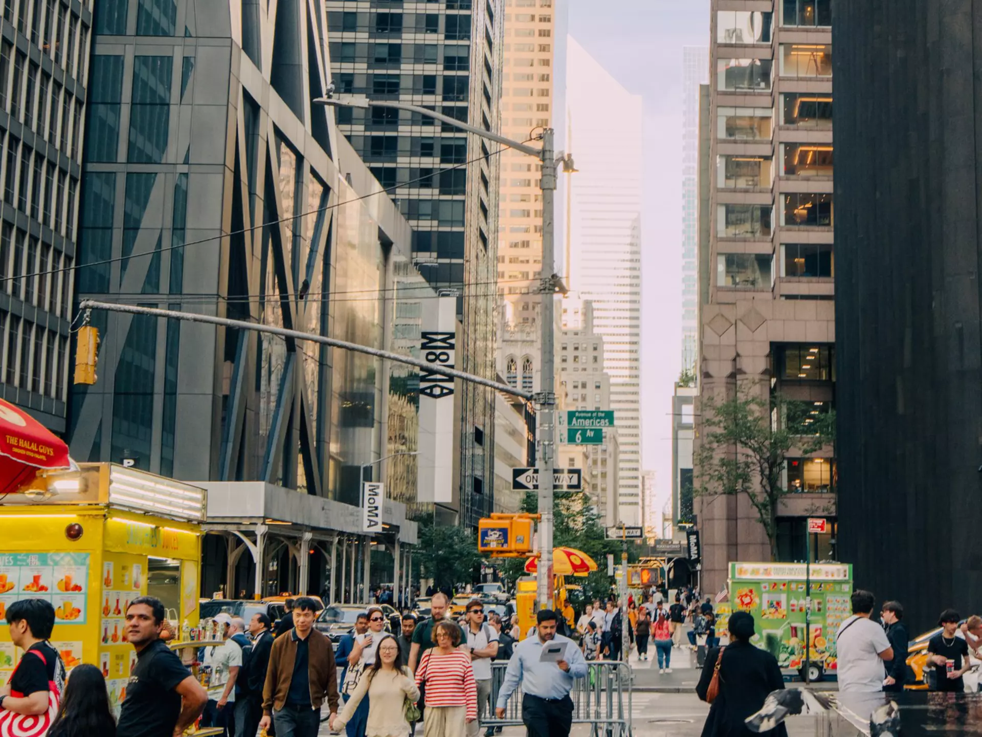 People walk past sculptures and skyscrapers on a city street