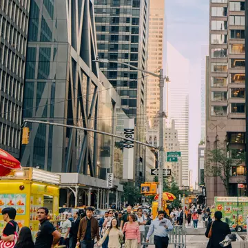 People walk past sculptures and skyscrapers on a city street