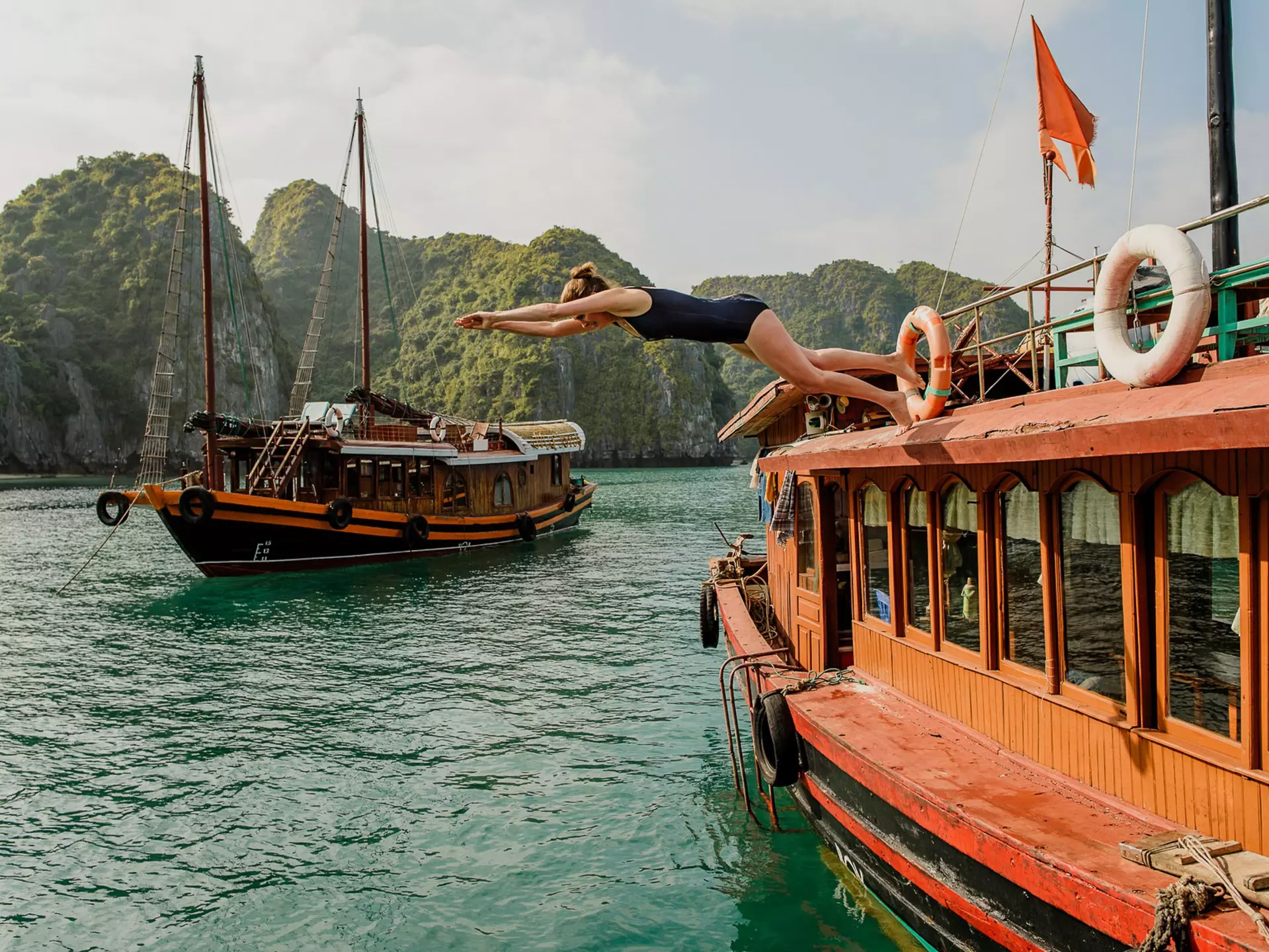 A woman dives off a boat in a bay with vast limestone outcrops