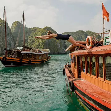 A woman dives off a boat in a bay with vast limestone outcrops