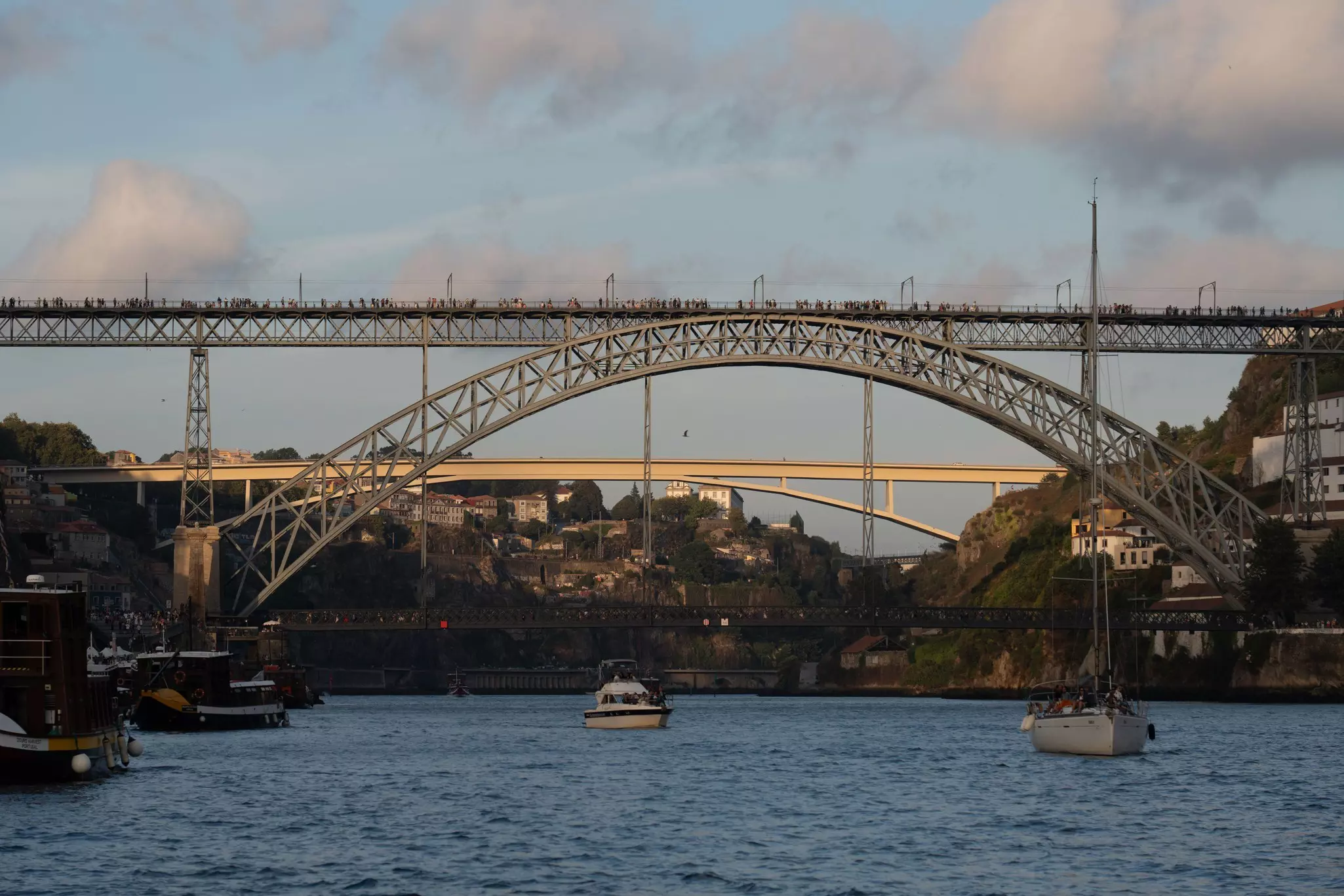 Boats pass under the Dom Luis I Bridge in Porto at sunset, Portugal.