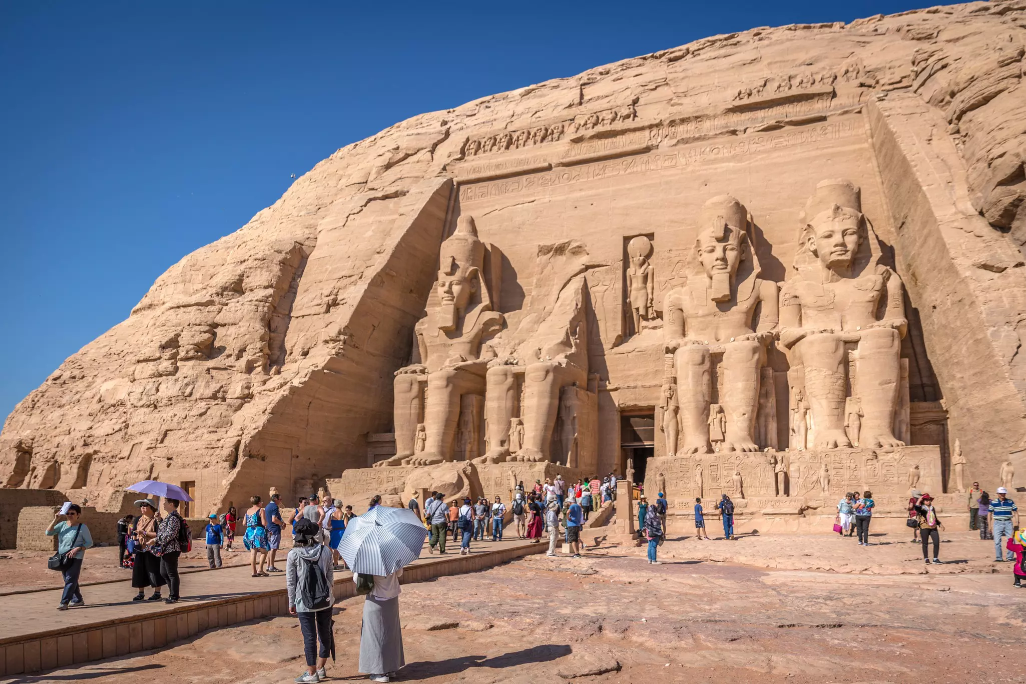 Big group of tourists in front of the large statues at Abu Simbel temple in southern Egypt in a blue sky day,