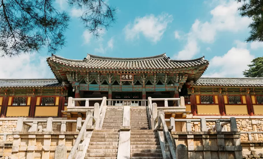 Twin stone stairways rising to the painted Jahamun gate of Bulguksa Temple, pine branches overhead, Gyeongju, South Korea