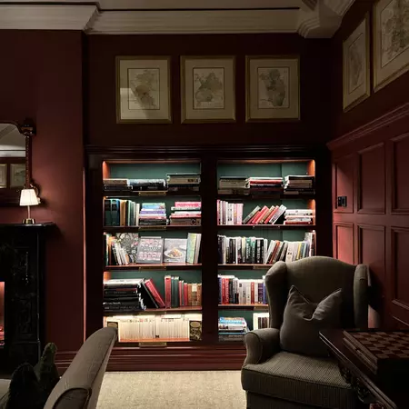 An armchair in front of a bookcase with interior lights on the shelves.