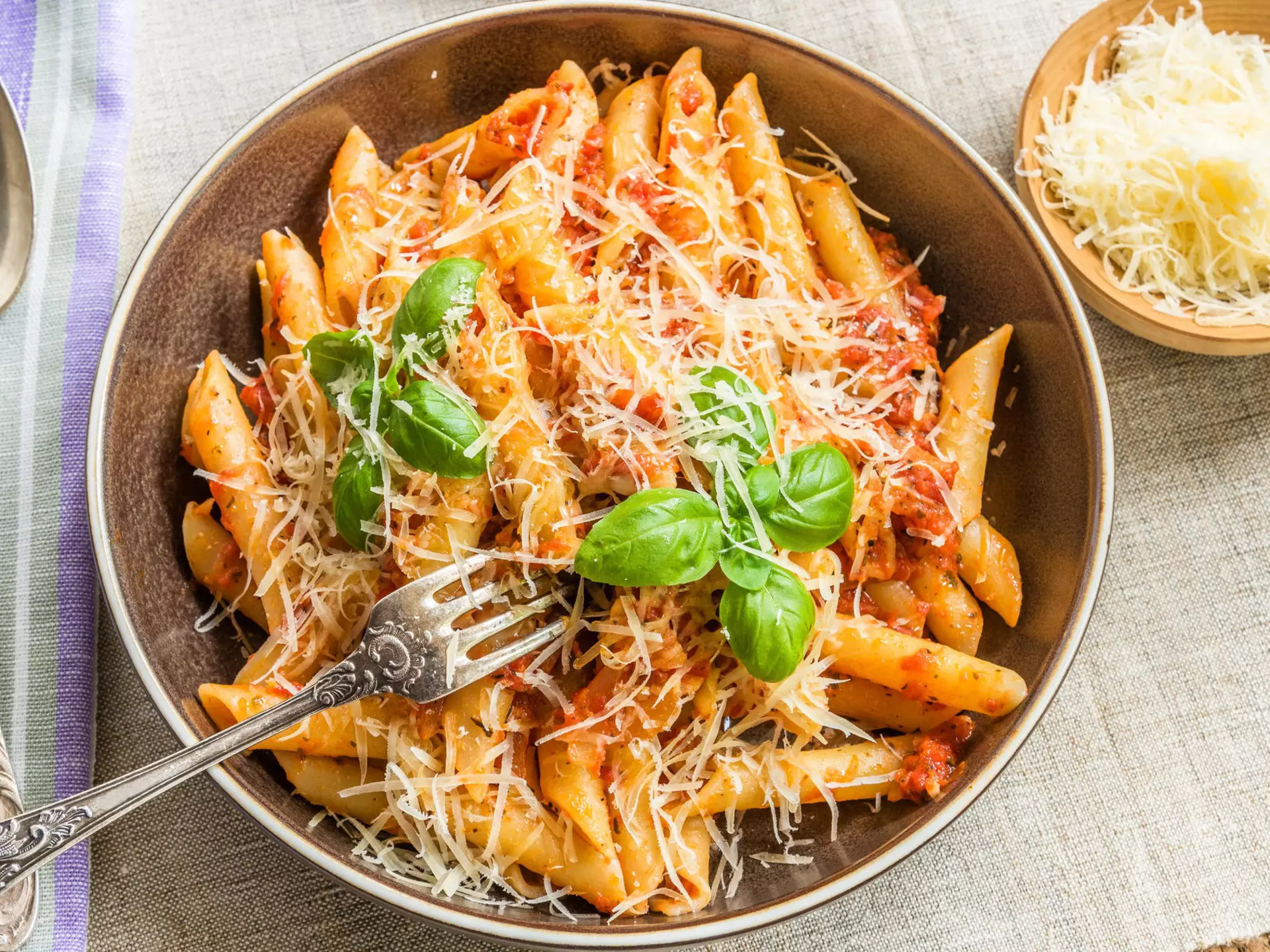 An overhead shot of a bowl of pasta with thinly grated cheese on top