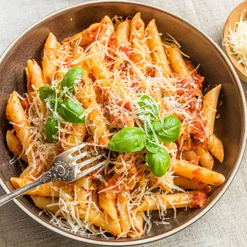 An overhead shot of a bowl of pasta with thinly grated cheese on top