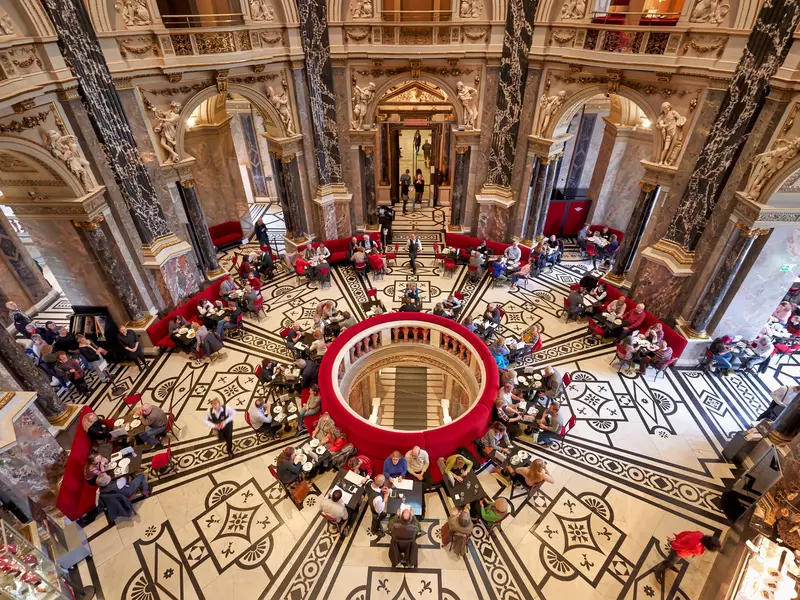 A cafe set in a rotunda in a museum in Vienna, with a patterned tile floor and red booths.