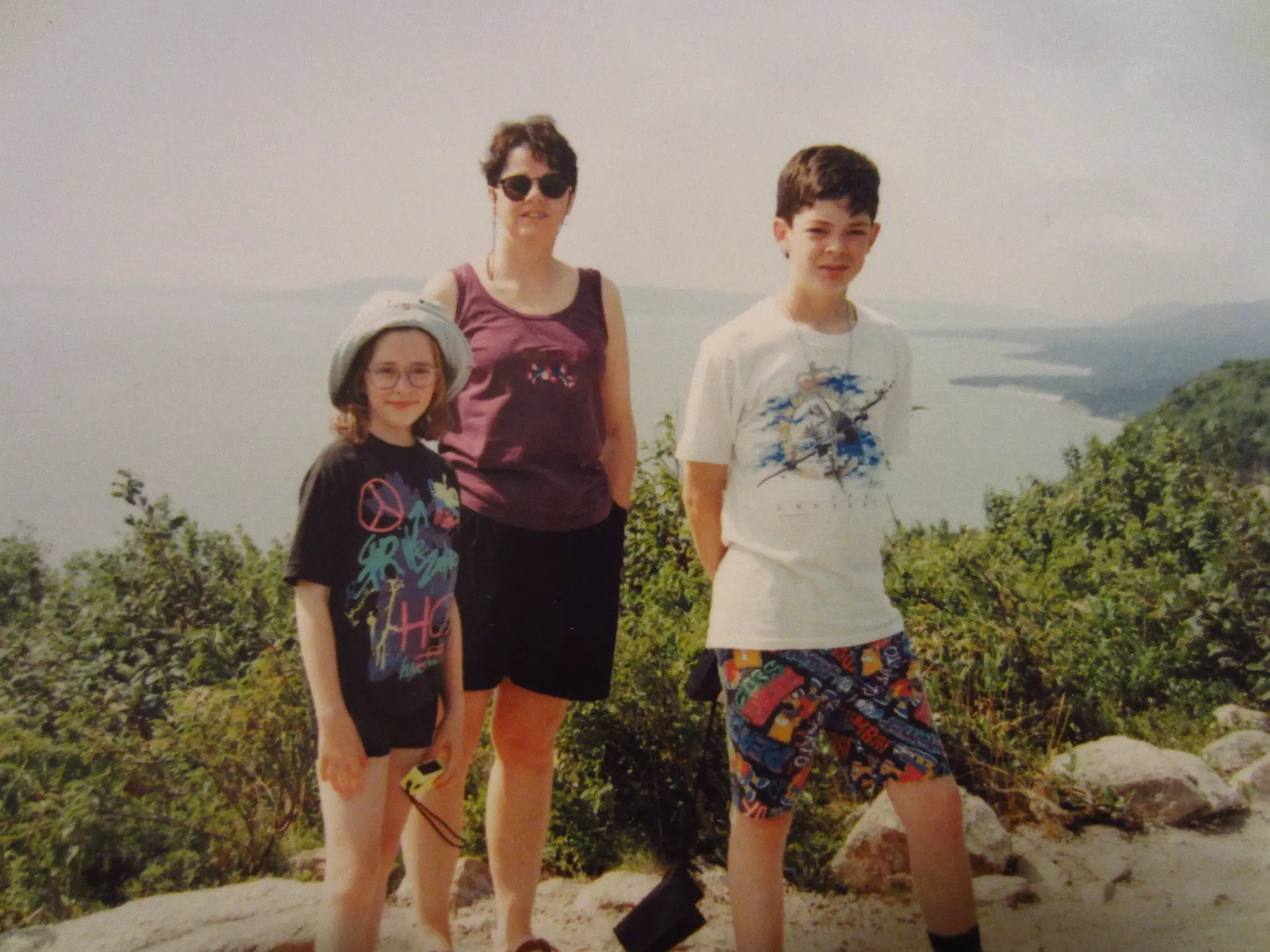 An older photo of a woman and two children standing a on cliff above the ocean.