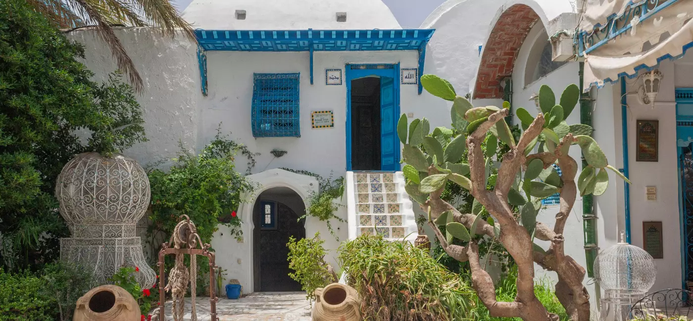 A whitewashed building with blue windows; large pottery vessels are on the patio, and tile steps lead to a blue door under a blue portico.