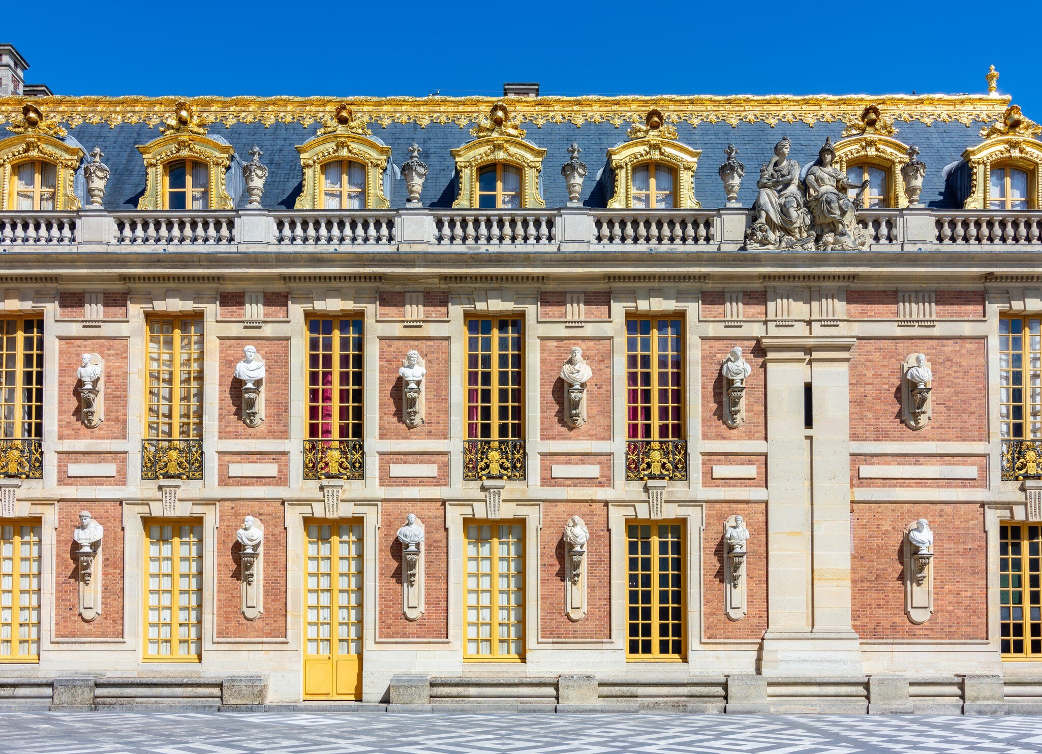 The façade of the Palace of Versailles featuring a combination of red brick, white stone and grey slate, highlighted by marble busts.