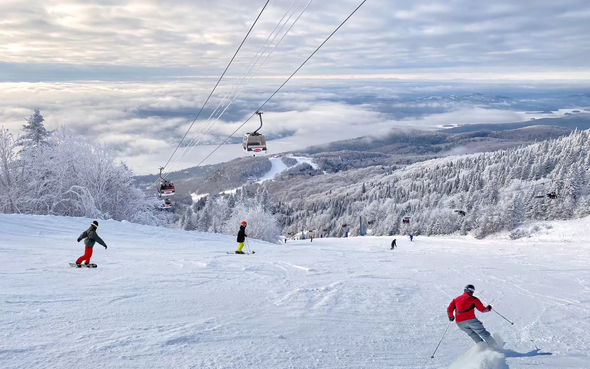 Skiers are pictured on a groomed trail at a ski resort as the cars of a gondola ascend above them, Mont Tremblant, Québec, Canada.