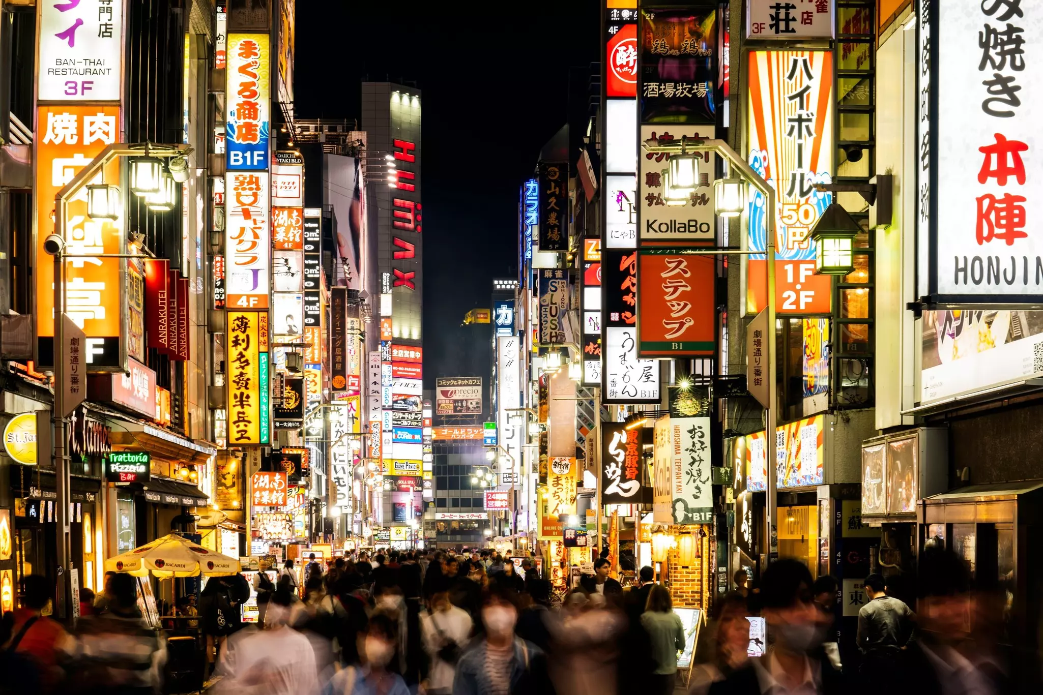 Crowds pass under neon lights in the Shinjuku district of Tokyo, Japan.