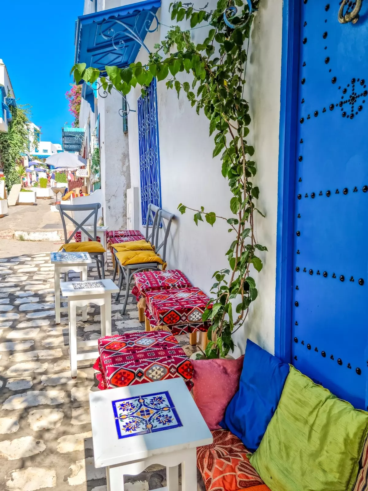 Chairs and stools decorated with colorful patterned textiles are set up on a cobblestone street.