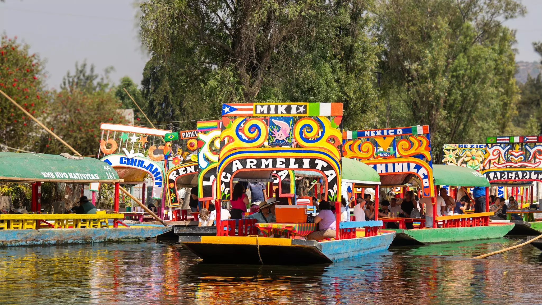 Colorful flat-bottomed boats on a canal, featuring live mariachi bands and a festival atmosphere