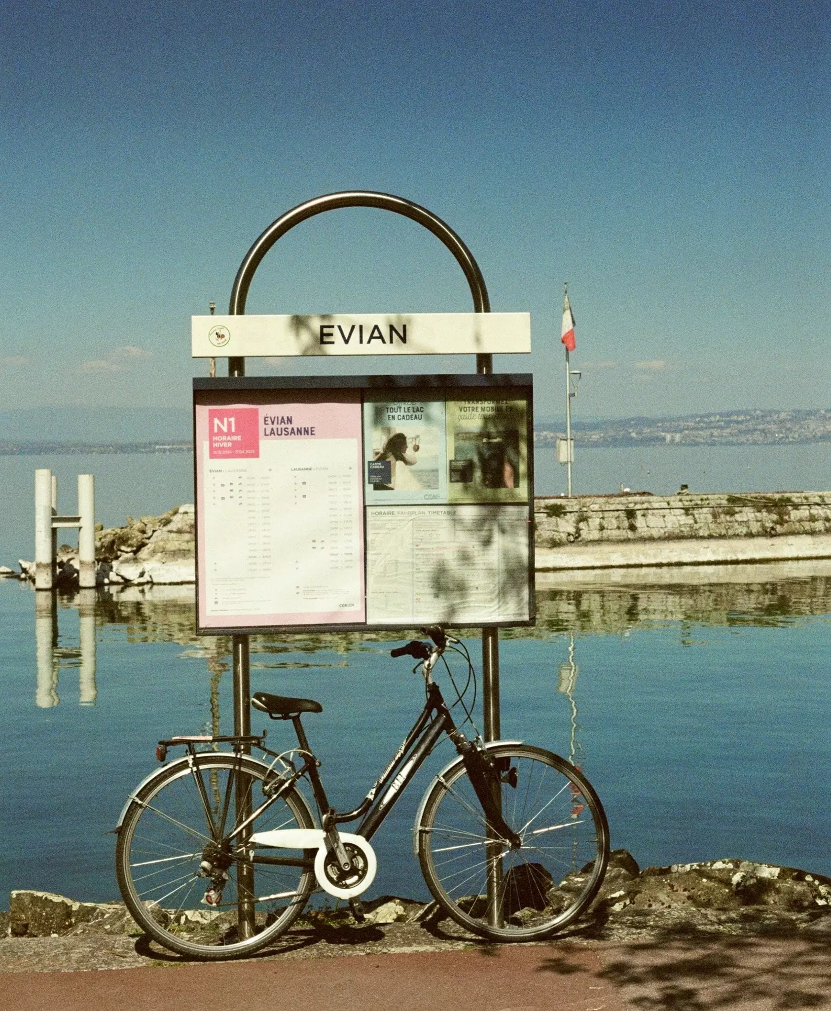 A bicycle leaning against a sign that reads "Evian" beside a lake