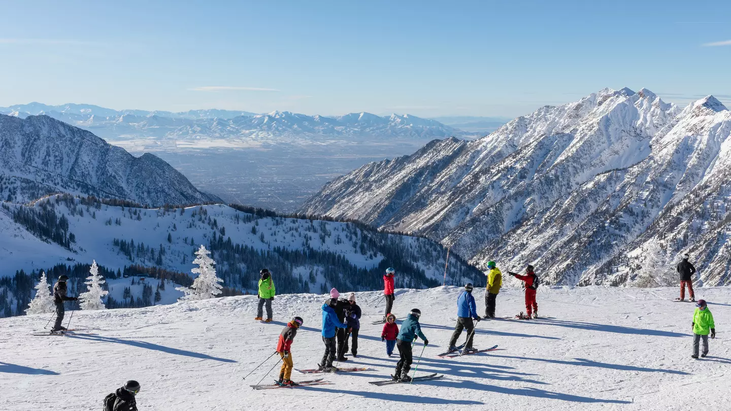 Skiers and snowboarders on top of a snowy peak with mountains stretching into the distance
