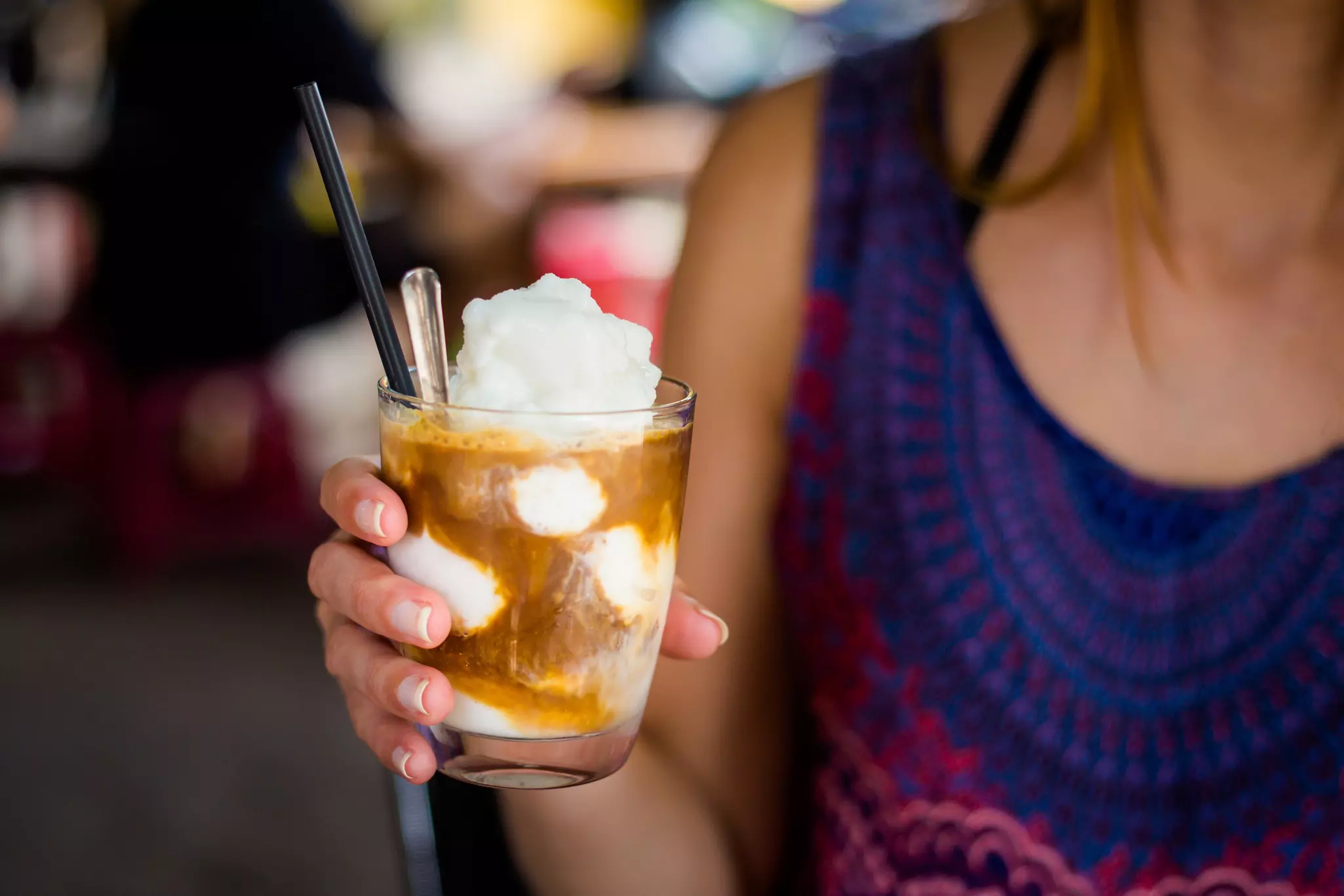 A woman's hand holds a glass of coffee with whipped coconut.