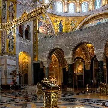 Gilded lectern on a patterned marble floor below mosaic saints, carved arcades and a ring of dome windows