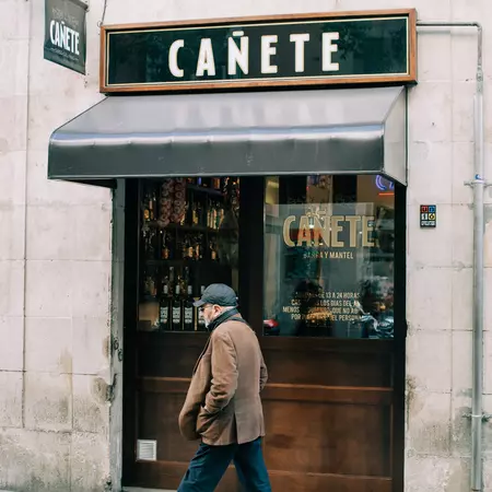 A senior man walking alone in front of a restaurant called Cañete 