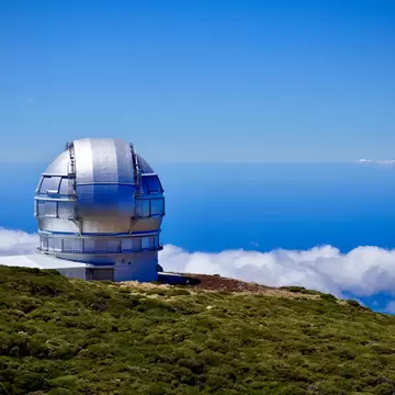Silver telescope dome on a green mountain ridge above a sea of clouds at Roque de los Muchachos Observatory, La Palma