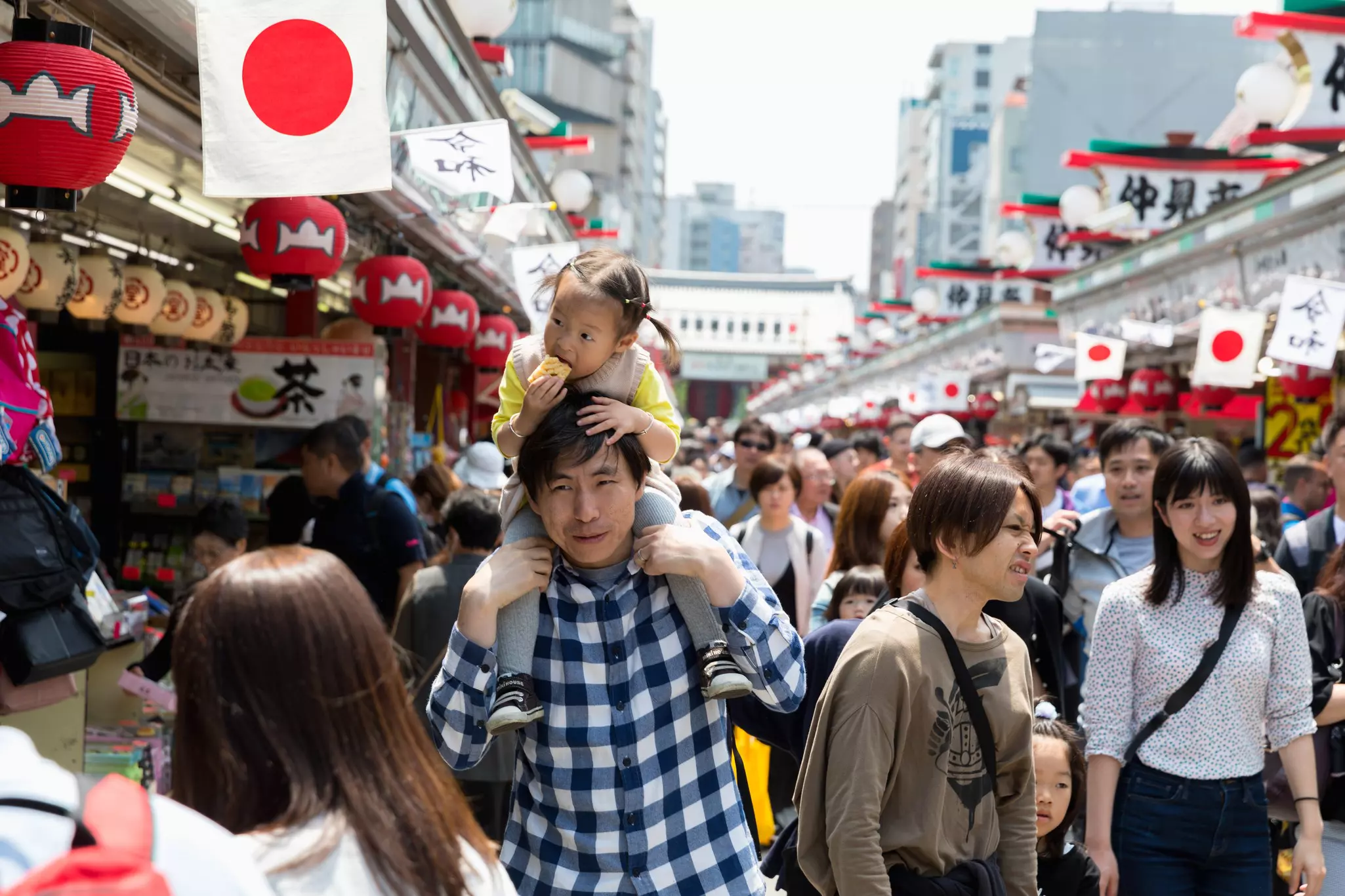 Shoppers on Nakamise-dōri in Tokyo; a man is carrying a girl on his shoulders at the center of the crowd.