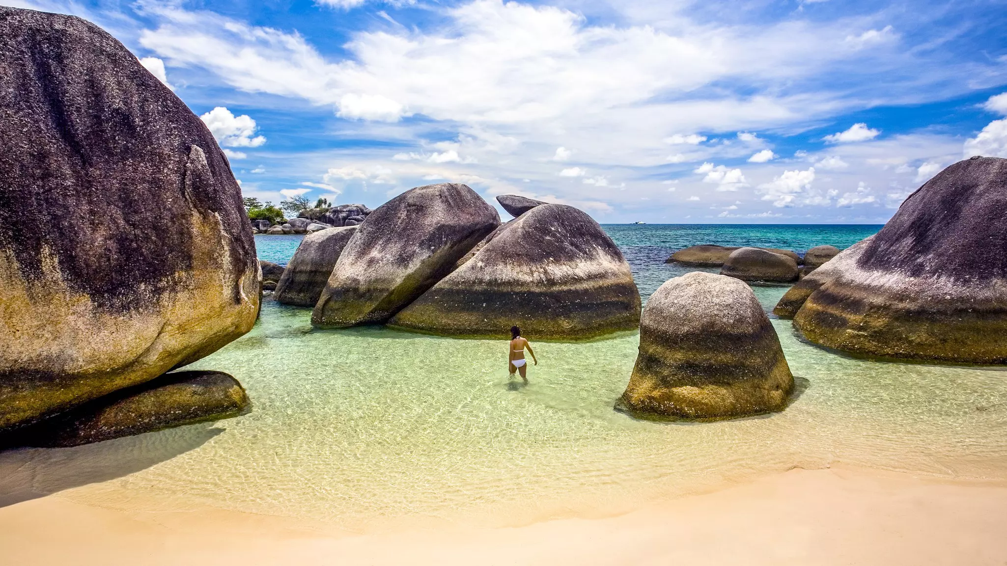 A woman wading in shallow water at beach with granite boulders at Bangka-Belitung, Belitung Island, Indonesia