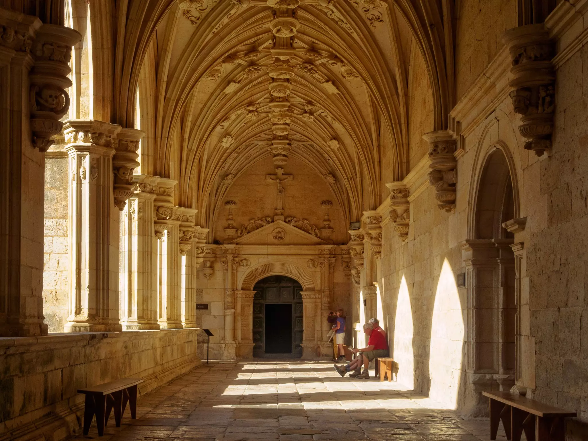 Pilgrims rest on a stone bench in a cloister of a basilica