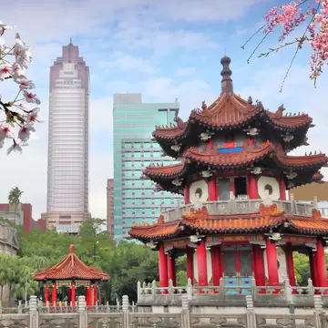 Springtime cherry blossoms in front of red pagodas and high-rise buildings in 2-28 Memorial Peace Park in Taipei, Taiwan.