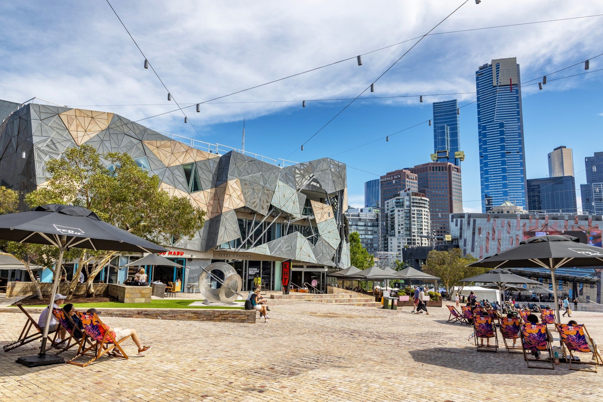 People enjoy the summer weather in Federation Square, Melbourne, Australia. The modern cultural centre is a hub for the arts, and is lively with bars and cafes. 