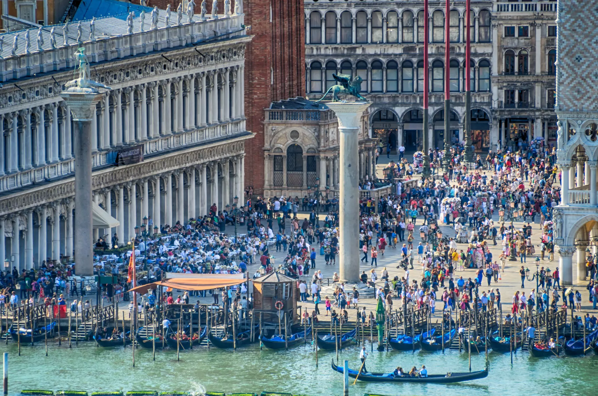 An aerial view of people filling a city plaza fronted by two columns on the waterfront