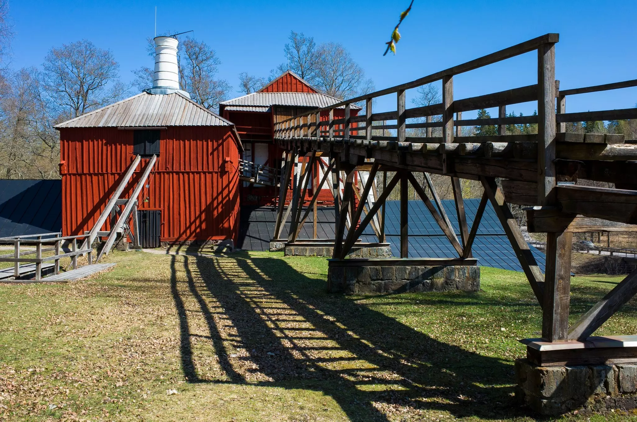 A wooden causeway leads to the red-painted buildings of a historic ironworks, located in a rural setting.