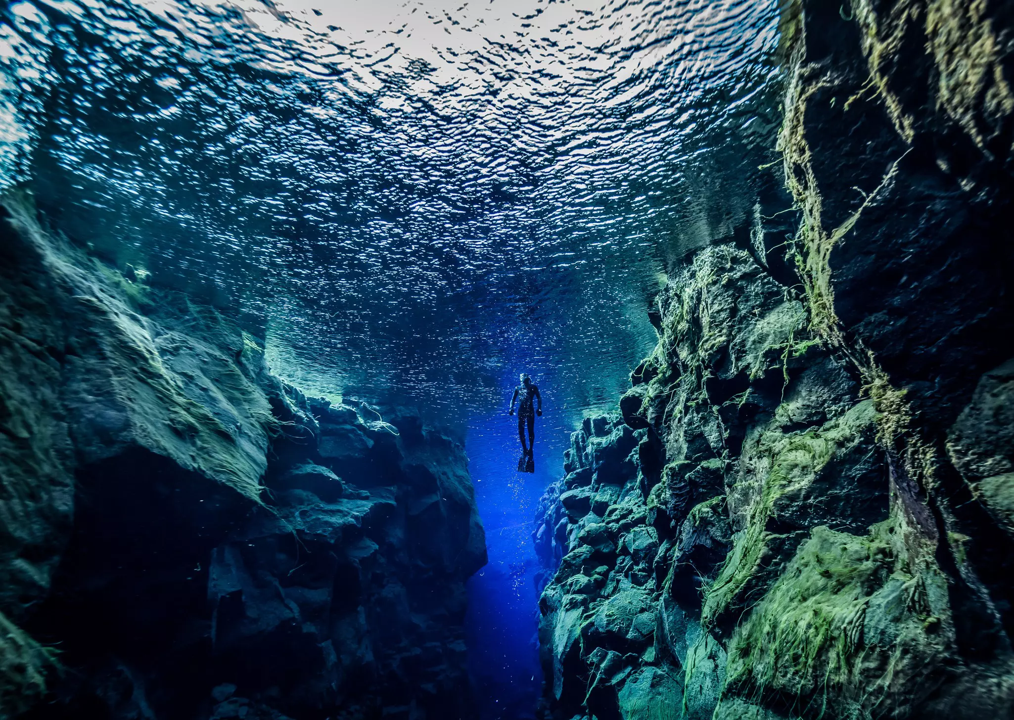 An underwater fissure with excellent visibility. A snorkeler floats at the surface.