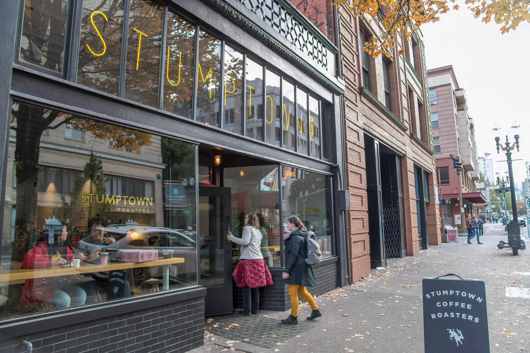 Two women walking into a coffee shop. A placard in front says Stumptown Coffee Roasters.