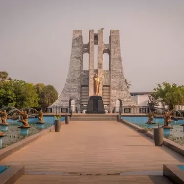 Tall grey marble monument with a gilded statue, reached by a walkway between fountains lined with bronze figures.