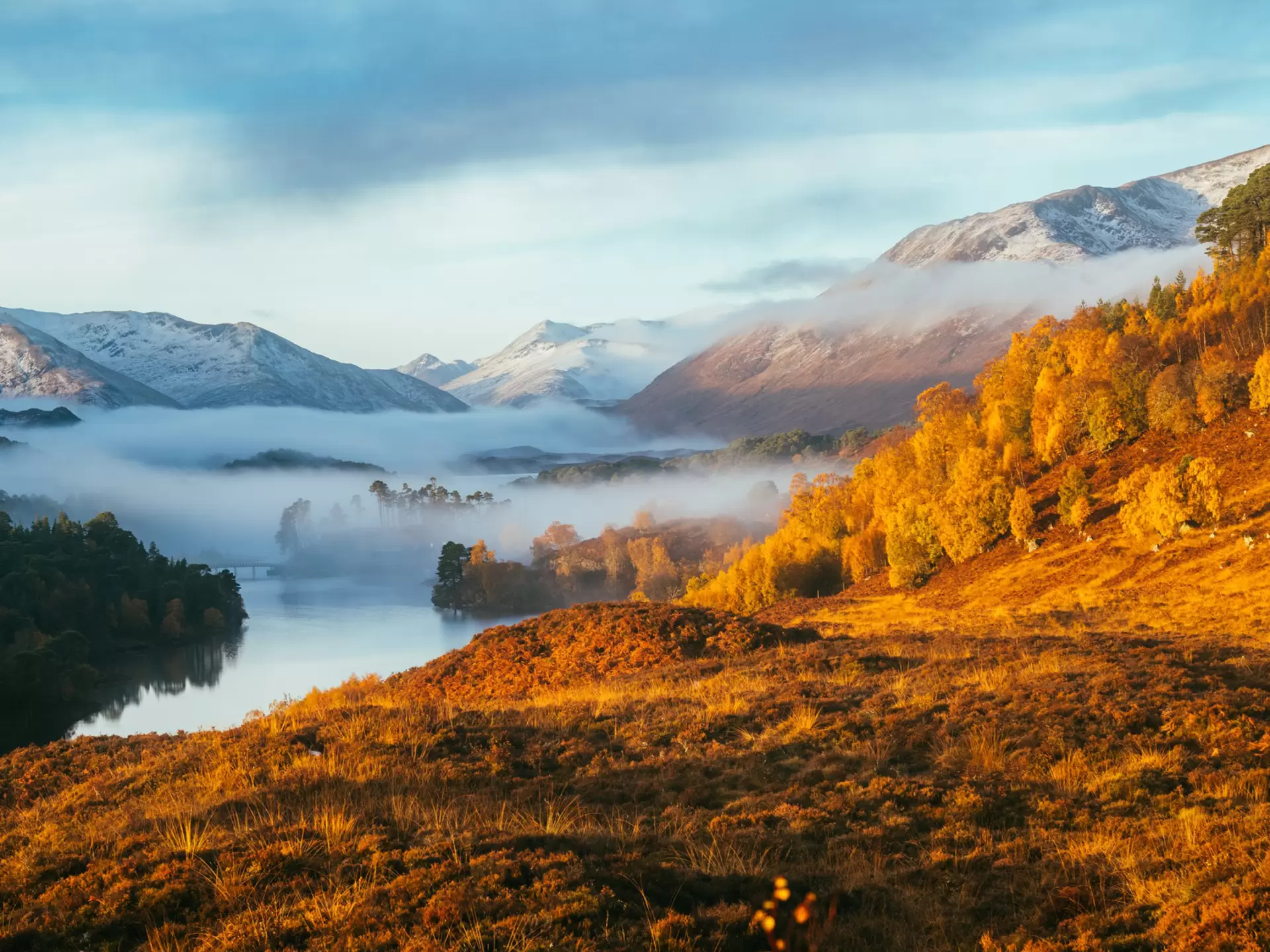 Autumn mist rolls in over Loch Affric in the Scottish Highlands, surrounded by hills glowing gold in the sunlight.