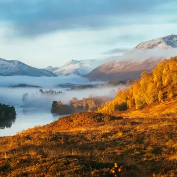 Autumn mist rolls in over Loch Affric in the Scottish Highlands, surrounded by hills glowing gold in the sunlight.