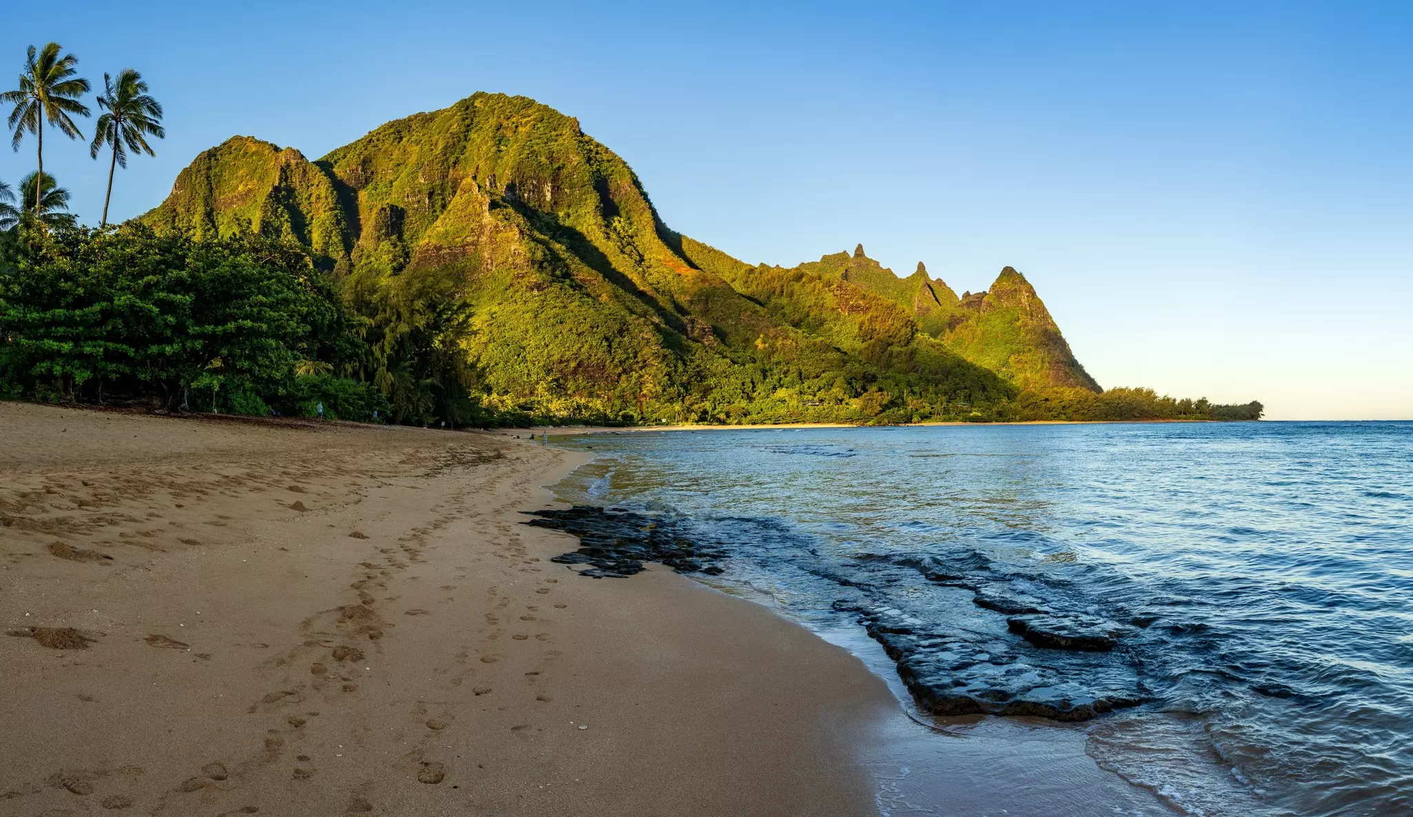 A beautiful sandy beach overlooked by vast greenery-covered peaks: Tunnels Beach on the Nāpali Coast, Kauaʻi.