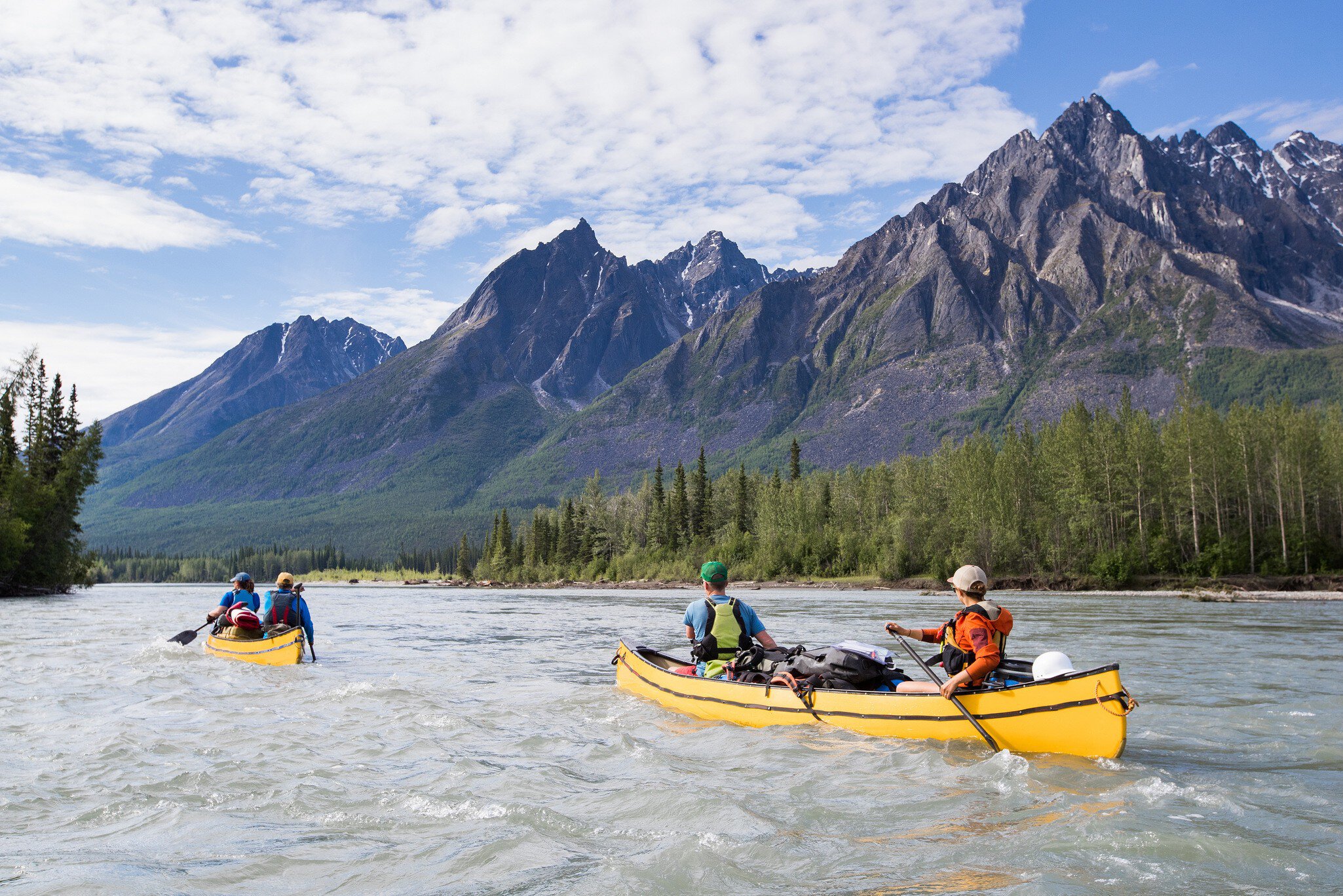 People in two canoes paddle down a river in a mountainous region.