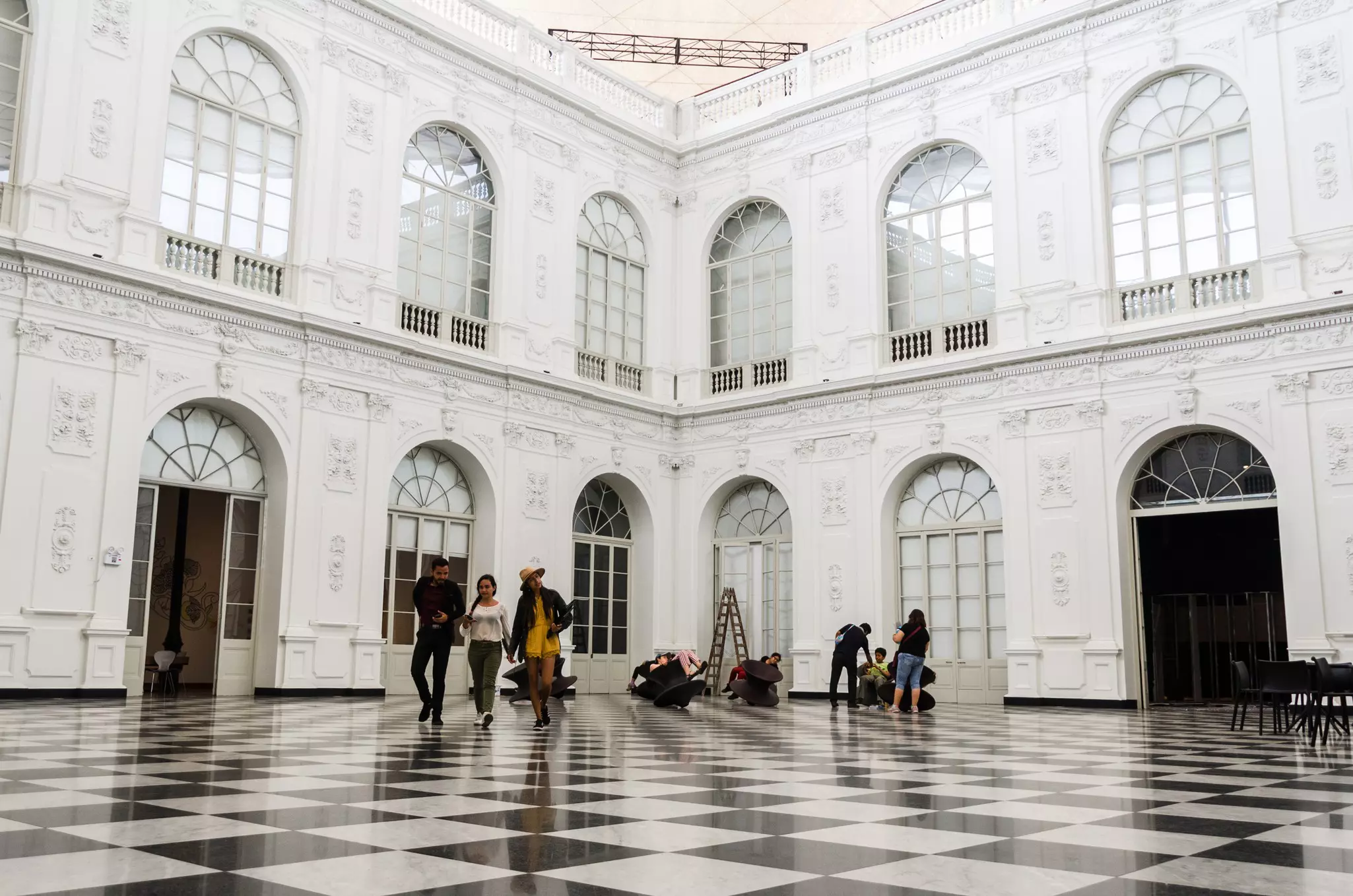 People walking in a large room with white walls, large windows, and a black and white checkered floor