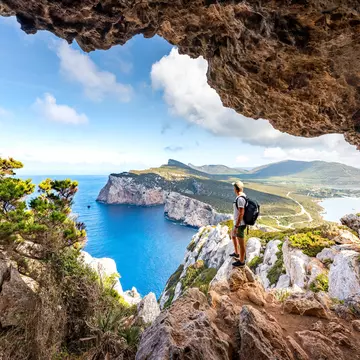Capo Caccia, hiker admiring the view from a cave. Sardinia island, Italy