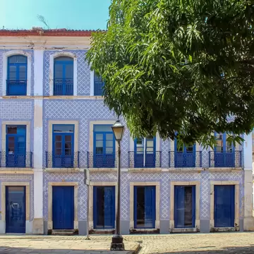 Building covered in blue and white tiles with blue shutters, a mango tree and cobbled street in Sao Luis, Brazil