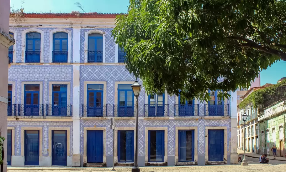 Building covered in blue and white tiles with blue shutters, a mango tree and cobbled street in Sao Luis, Brazil