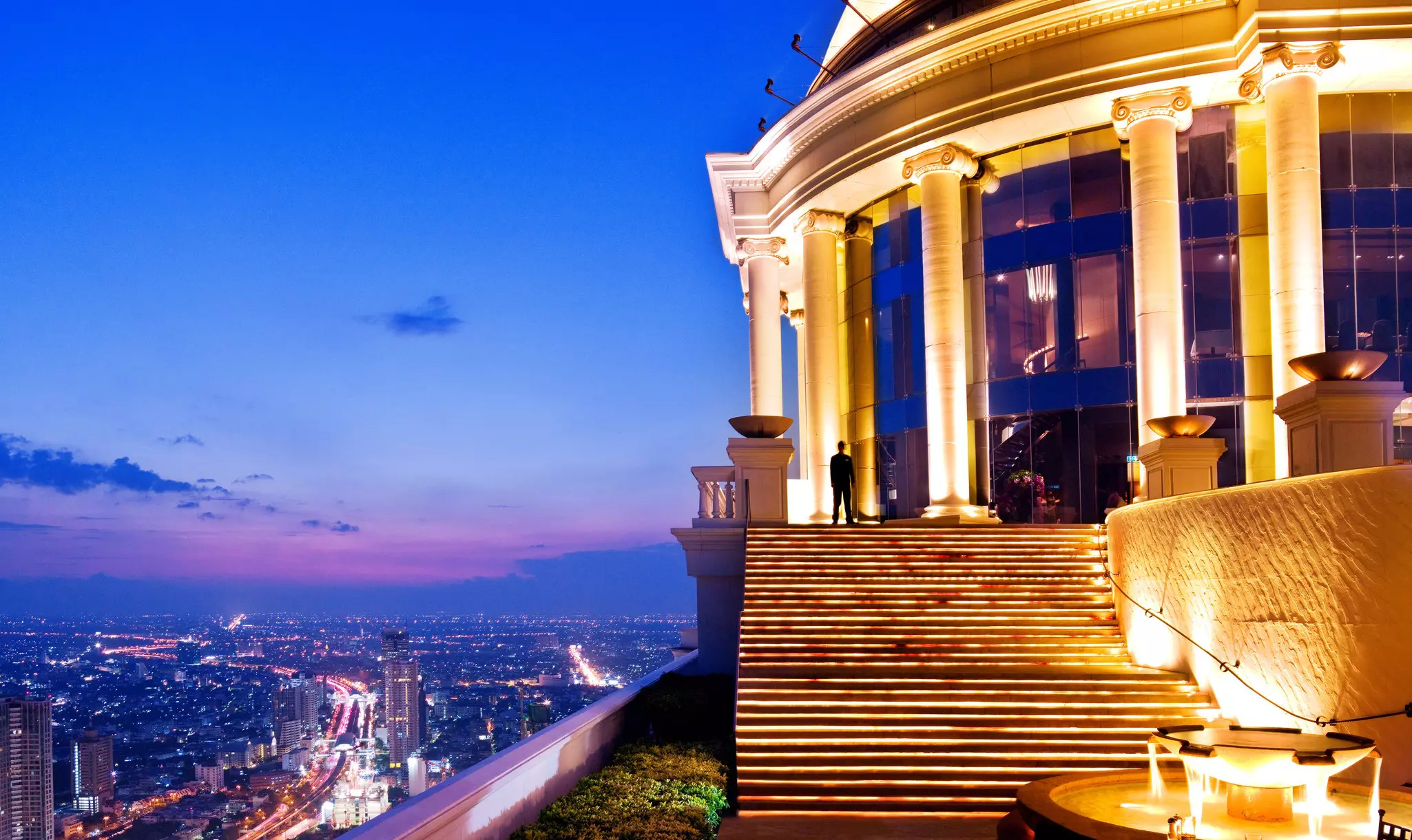 A stairway leading up from a rooftop terrace to an indoor bar with long-distance of the city below